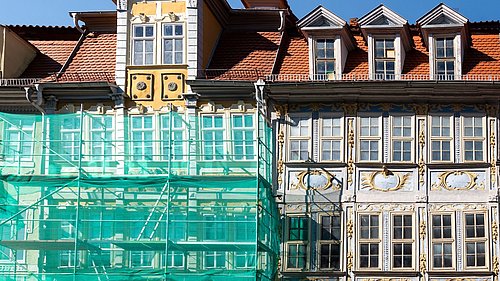 Foto, Fassaden zweier historischer Gebäude mit Satteldächern, eines teilweise mit grünem Gerüst verhüllt.