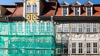 Foto, Fassaden zweier historischer Gebäude mit Satteldächern, eines teilweise mit grünem Gerüst verhüllt.