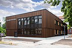 Foto, Außenansicht von zweistöckigem Gebäude mit dunkler Holzverkleidung. 