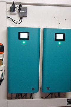 Foto, Inneneinheit der Wärmepumpenkaskade, Technikraum mit zwei blauen Steuergeräten an der Wand, mehreren Rohrleitungen und Ventilen