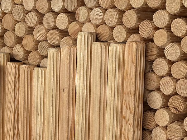 Foto, Mehrere runde Holzstäbe liegen dicht nebeneinander, darauf liegen längliche, geriffelte Holzleisten in unterschiedlicher Höhe.