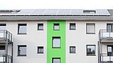 Foto, modernes Gebäude mit grüner Akzentwand und Sonnenkollektoren auf dem Dach, mit mehreren Balkonen und Fenstern.