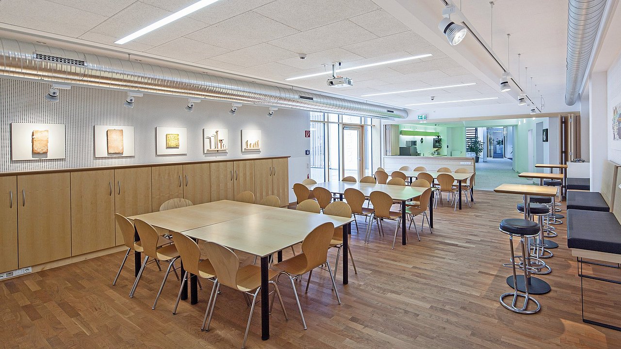 Foto, Moderner Aufenthaltsraum mit mehreren Tischen und Stühlen, Holzfußboden und beleuchteten Bildern an der Wand