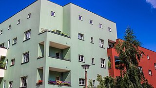 Foto, mehrstöckiges Wohngebäude mit Balkonen, umgeben von Bäumen und unter blauem Himmel