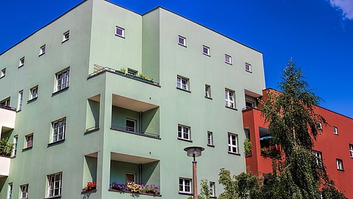 Foto, mehrstöckiges Wohngebäude mit Balkonen, umgeben von Bäumen und unter blauem Himmel