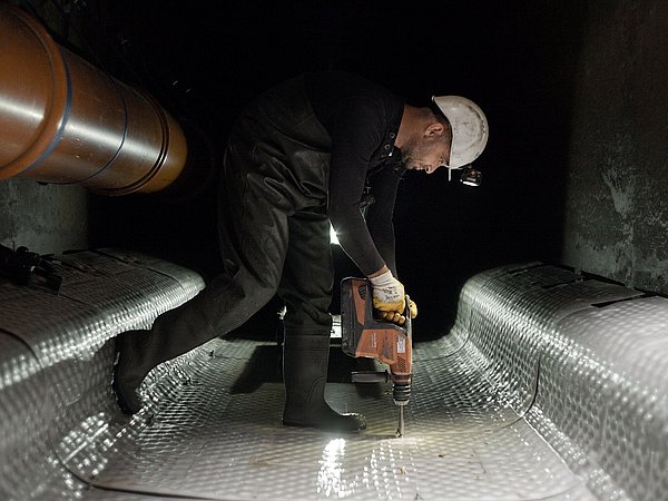 Foto, ein Arbeiter mit Helm steht in einem Tunnel und bohrt in den Boden.