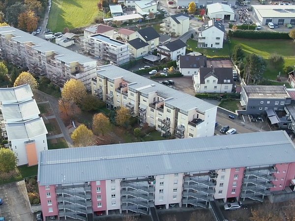 Luftaufnahme eines Wohngebiets mit mehrstöckigen Gebäuden, Bäumen mit Herbstlaub und Straßen mit parkenden Autos