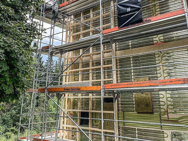 Foto, Fassade eines mehrstöckigen Gebäudes mit Gerüst und Dämmmaterial, umgeben von Bäumen