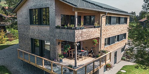 Foto, Außenansicht auf Zweifamilienhaus mit Terrasse, Balkon und Photovoltaik-Kollektoren auf dem Dach.