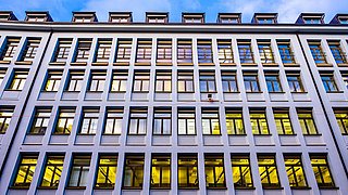 Foto, Fassade eines mehrstöckigen Bürogebäudes mit vielen beleuchteten Fenstern in regelmäßigen Reihen