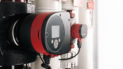 Foto, Nahaufnahme eines runden, schwarzen und roten elektronischen Geräts mit Display und Tasten an einer Rohrleitung.