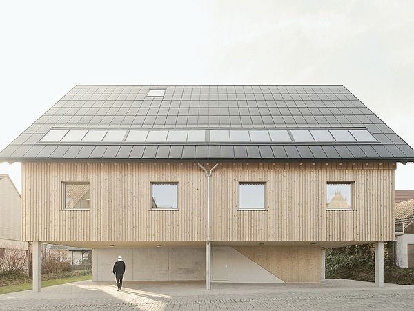 Foto, Modernes zweistöckiges Holzhaus auf Stelzen mit großem, geneigtem Solardach und drei rechteckigen Fenstern