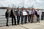 Foto, Gruppenbild mehrerer Personen, die nebeneinander an einem Geländer lehnen. Dahinter befindet sich ein Fluss und der Hamburger Hafen.