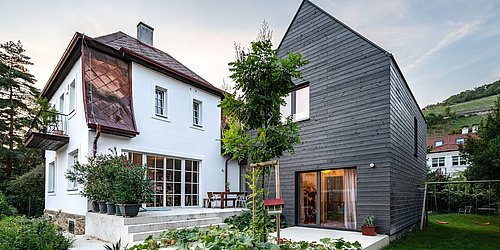 Foto, Modernes Haus mit weißem Altbau und neuem Anbau aus dunklem Holz, Garten mit Gemüsebeeten und Terrasse