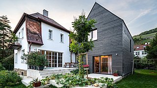 Foto, Modernes Haus mit weißem Altbau und neuem Anbau aus dunklem Holz, Garten mit Gemüsebeeten und Terrasse