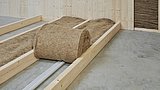 Foto, Rolle aus brauner Schafwolle zur Bodenisolierung auf Betonboden mit Holzkonstruktion und Rohrleitungen