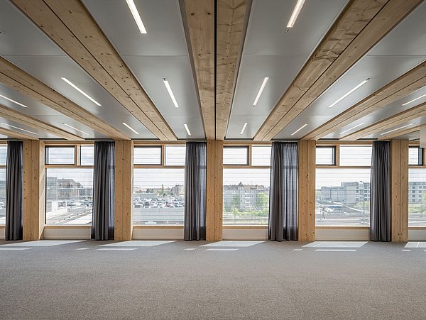 Foto, Innenraum mit Teppichboden, Fensterfront und Gardinen sowie eine Decke aus Holz und Beton.