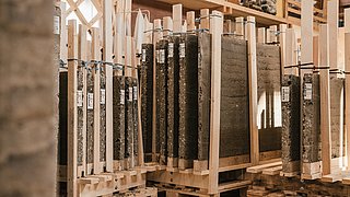 Foto, mehere vorgefertigte Bauelemente aus Stampflehm stehen in zur Trocknung in einer Werkhalle.
