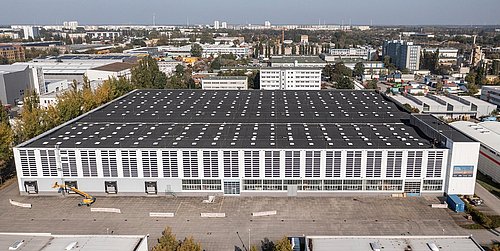 Foto, Luftaufnahme einer Fabrikhalle mit einer PV-Anlage auf dem Dach und Solarfolien an der Fassade.