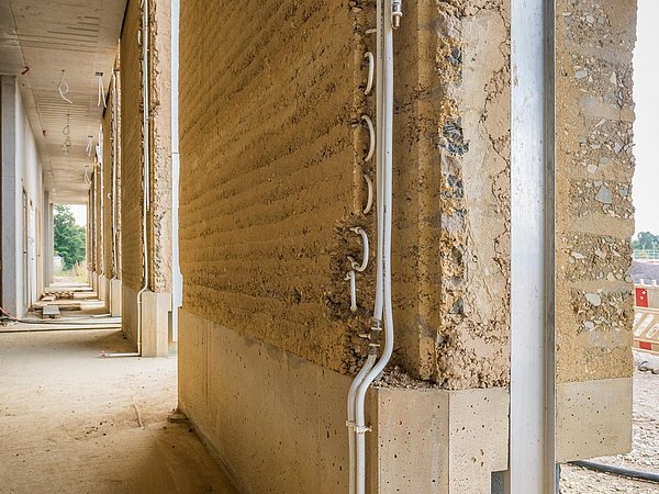 Foto, im Bau befindliche Stampflehmfassade durch die die Leitungen der Wandheizung führen.