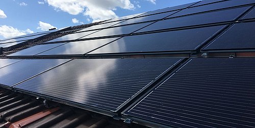 Foto, Schwarze PVT-Solarkollektoren auf einem Ziegeldach unter blauem Himmel mit Wolken