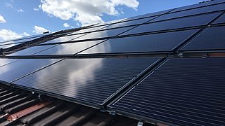 Foto, Schwarze PVT-Solarkollektoren auf einem Ziegeldach unter blauem Himmel mit Wolken