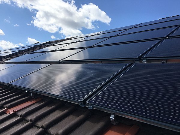 Foto, Schwarze PVT-Solarkollektoren auf einem Ziegeldach unter blauem Himmel mit Wolken