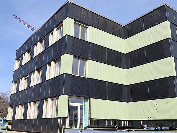 Foto, Modernes Bürogebäude in Bau mit schwarzer und grüner Fassade, mehreren Fenstern und Baustelle im Vordergrund