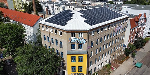 Foto, Dreigeschossiges Gebäude mit Solarpaneelen auf dem Dach und Graffiti an der Fassade in einer Wohngegend