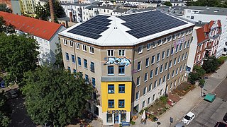 Foto, Dreigeschossiges Gebäude mit Solarpaneelen auf dem Dach und Graffiti an der Fassade in einer Wohngegend