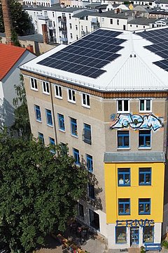 Foto, Dreigeschossiges Gebäude mit Solarpaneelen auf dem Dach und Graffiti an der Fassade in einer Wohngegend