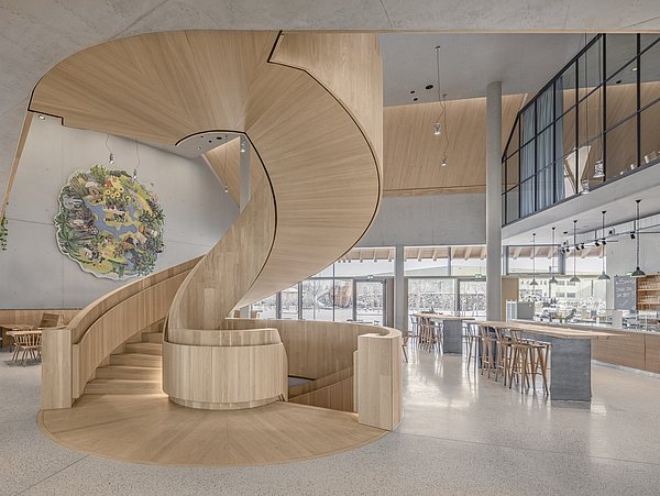 Foto, Große spiralförmige Holztreppe in einem Besucherzentrum mit Cafébereich und großem Wandbild