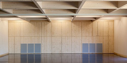 Foto, großer Innenraum mit dunklem Boden, Holzwänden und Holzdecke mit Balken. 