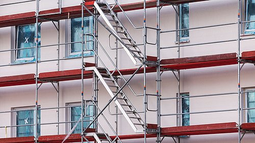 Foto, Fassade eines mehrstöckigen Gebäudes mit Gerüst und Treppe davor.