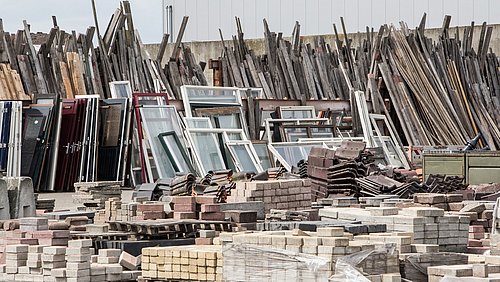 Foto, ein Bauhof mit gebrauchten Ziegelsteinen, Fenstern und anderen Baumaterialien und Bauteilen.