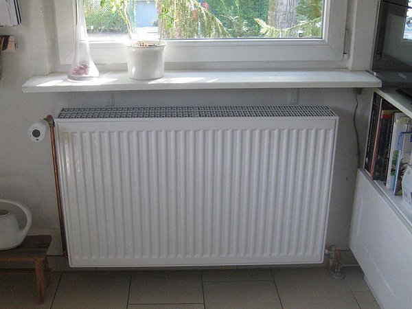 Foto, Moderner weißer Heizkörper unter einem Fenster in einem Raum mit Fliesenboden und Bücherregal