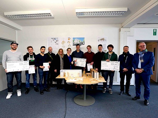 Foto, Gruppe von Menschen stehen in einer Reihe hinter einem architektonischen Model. Einige Personen halten PR-Checks aus Pappe.