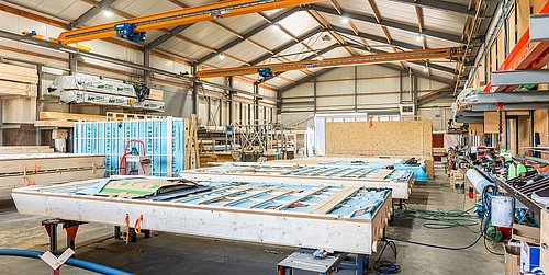 Foto, eine große Produktionshalle mit Holzkonstruktionen, Kränen und Arbeitsmaterialien für die Fertigung.