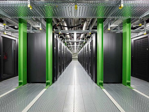 Foto, Rechenzentrum mit Reihen von schwarzen Server-Racks und grünen Stützsäulen, metallischer Boden und Decke mit Kabeltrassen