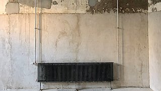 Foto, ein an einer Betonwand hängender gebrauchter Heizkörper, welcher in einem neu gebauten Gebäude wiederverwendet wurde.