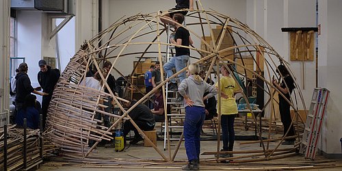 Foto, mehrere Personen arbeiten an einer Holzkonstruktion in Kuppelform