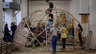 Foto, mehrere Personen arbeiten an einer Holzkonstruktion in Kuppelform