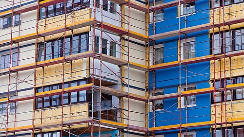 Foto, Nahaufnahme eines mehrstöckigen Wohngebäudes mit Baugerüst, bei dem die Fassade gedämmt wird.