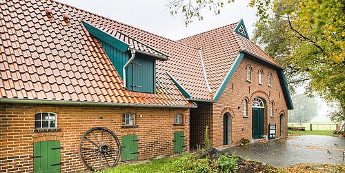 Foto, Außenansicht eines Niedersachsenhauses mit Klinkerfassade und grünen Details.