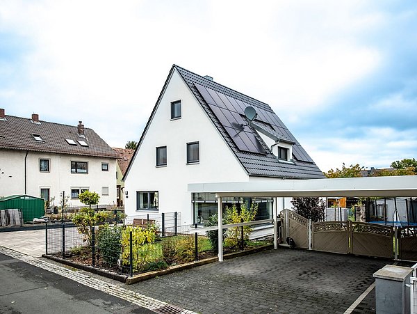 Foto, Einfamilienhaus mit Carport, Garten und Photovoltaikanlage auf dem Dach. 