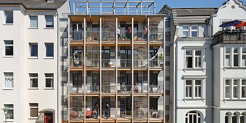 Foto, Straßenfassade mit moderner Holzverkleidung und Balkonen zwischen zwei traditionellen mehrstöckigen Gebäuden