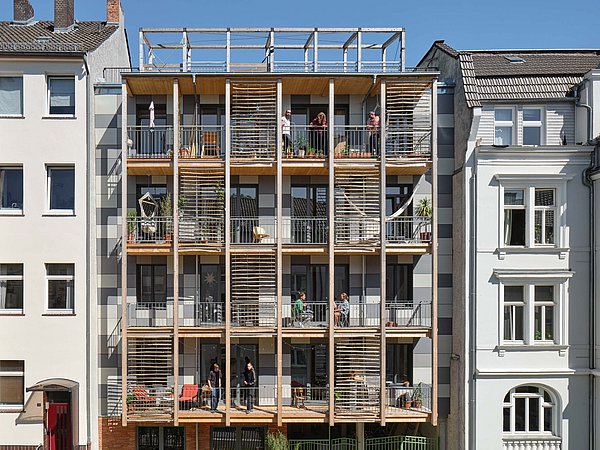 Foto, Straßenfassade mit moderner Holzverkleidung und Balkonen zwischen zwei traditionellen mehrstöckigen Gebäuden