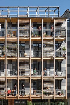 Foto, Straßenfassade mit moderner Holzverkleidung und Balkonen zwischen zwei traditionellen mehrstöckigen Gebäuden
