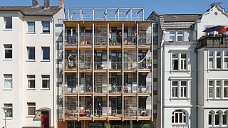 Foto, Straßenfassade mit moderner Holzverkleidung und Balkonen zwischen zwei traditionellen mehrstöckigen Gebäuden