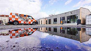 Foto, Oranger Recycling-Transporter mit Schriftzug 'Berlin Recycling' vor modernem Gebäude, Spiegelung im Wasserpfütze